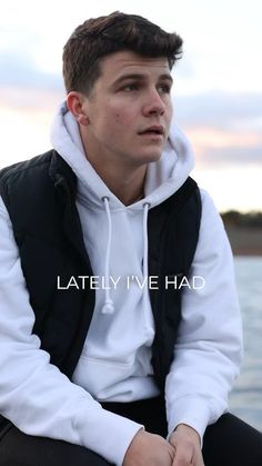 a young man sitting by the water wearing a white and black hoodie