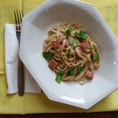 a white bowl filled with pasta and meat on top of a yellow place mat next to a fork