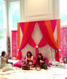 two women sitting on a bed with pink and orange drapes