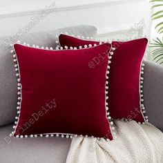 two red pillows sitting on top of a gray couch next to a white throw pillow