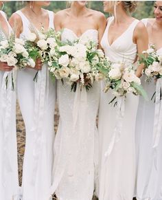 a group of women standing next to each other wearing white dresses and holding bouquets