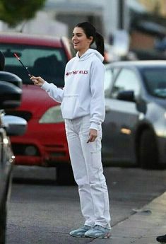 a woman in white is standing on the sidewalk with her hand out to another person