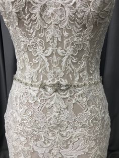 the back of a white wedding dress with an intricate lace pattern and beaded belt