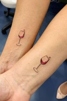 two people with matching tattoos on their arms holding wine glasses and one has a red wine glass in the other hand