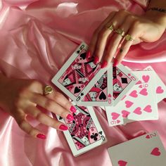 a woman's hands holding four playing cards on a pink satin sheeted surface