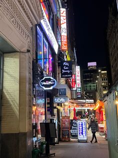 a city street at night with neon signs on the buildings and people walking down the sidewalk