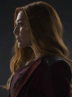 a woman with long red hair standing in front of a black background and looking off to the side