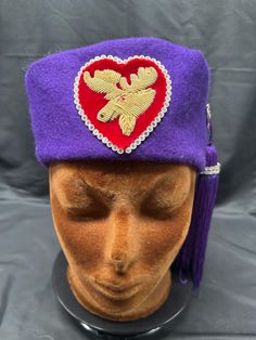 Vintage Royal Order of Moose Lodge Fez ceremonial cap oddity secret fraternity This is one amazing Vintage Moose Lodge Fez hat that is sure to make you the toast of the town. This darling and unique hat features: * lush purple, red, & gold colors * high quality 100% wool around the perimeter and a satiny material at the top * fez or pillbox style * from the royal order of the moose lodge (this is a fraternity that started in 1988) * front center has a sunning gold colored moose that was wire embroidered onto red velvet * the red velvet is heart shaped and has wire embroidered trim * the moose emblem is very striking and stands out beautifully * the left side of the hat has a tassel that hangs down and sways with movement * right side of the hat also has two pink Rhinestone hearts connected Fez Hat, Moose Lodge, Antique Collectors, Unique Hats, Gold Colors, Rhinestone Heart, Bucket Hats, Pink Rhinestones, Fraternity