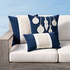 two blue and white pillows sitting on top of a wooden bench next to the ocean