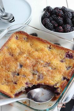 a close up of a casserole with berries in bowls on a table next to utensils