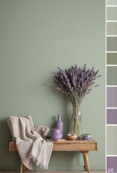 a wooden table topped with a vase filled with purple flowers next to a green wall