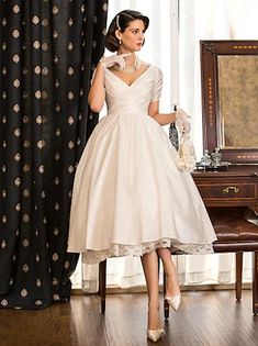 a woman standing in front of a mirror wearing a white dress with gold polka dots