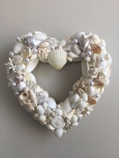 a heart shaped wreath made out of seashells and pearls hangs on the wall