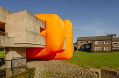 an inflatable orange object sitting on top of a grass covered field next to a building