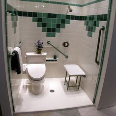 a white toilet sitting in a bathroom next to a walk in shower with green tile on the walls