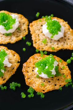 four crackers with peas and sour cream on them are sitting on a black plate