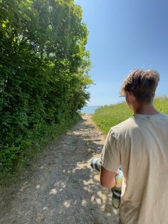 a man walking down a dirt road next to a lush green forest