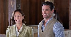 a man and woman standing next to each other in front of a barn with wooden walls