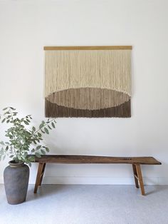 a wooden bench sitting next to a potted plant on top of a white wall