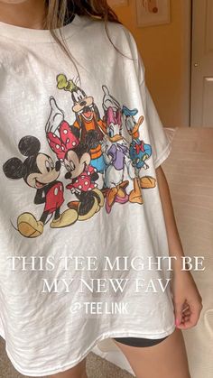 a woman wearing mickey mouse tshirt and shorts standing in front of a bed