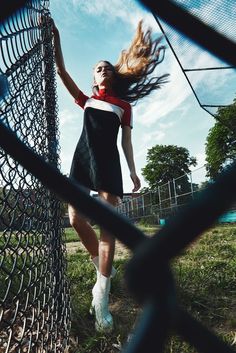 a woman in a black and white dress is standing by a fence with her hair blowing