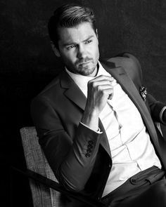 a black and white photo of a man sitting in a chair with his hand on his chin