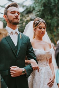 a man in a green suit standing next to a woman wearing a white dress and veil