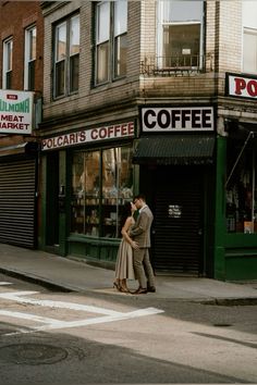 a man and woman are kissing in front of a coffee shop on the corner of a city street