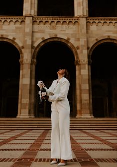 a woman standing in front of a large building holding a white cat and looking up at the sky