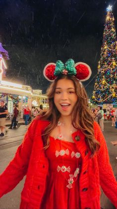 a woman wearing minnie mouse ears standing in front of a christmas tree at disneyland world