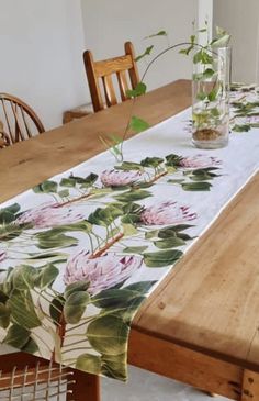 a wooden table topped with a glass vase filled with flowers next to a white table cloth