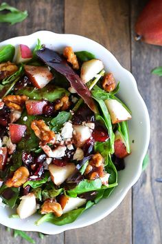 a white bowl filled with salad sitting on top of a wooden table next to an apple