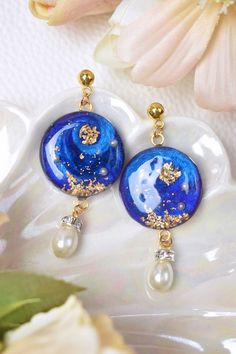 a pair of blue and white earrings with pearls on them, sitting next to flowers