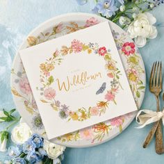 a wedding card on a plate next to some flowers and gold cutlery with the word wed me written in cursive