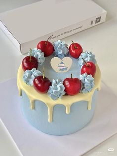 a blue cake with white icing and cherries on top, sitting in front of a box