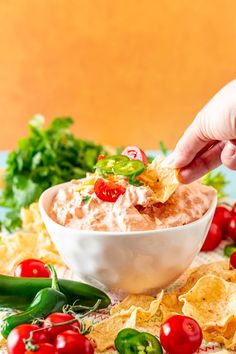 a person dipping salsa into a bowl with tortilla chips and tomatoes on the side