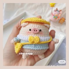 a hand holding a small crocheted pig wearing a yellow and blue hat with a bow on it's head