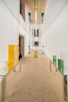 an empty hallway with yellow and green glass cases on either side of the hall, and a person standing in the doorway