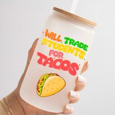 a woman holding up a plastic cup that says will trade students for tacos on it