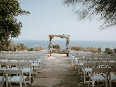 an outdoor ceremony set up with white chairs and greenery on the aisle, overlooking the ocean