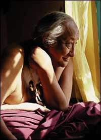 an older woman laying on top of a bed next to a white curtain and window