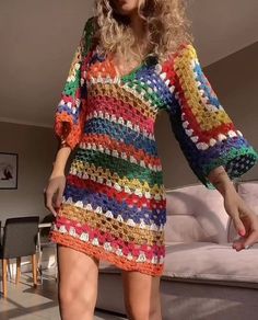 a woman in a multicolored crocheted dress is posing for the camera