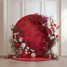 a red circle with flowers on it in front of a white wall and wooden floor