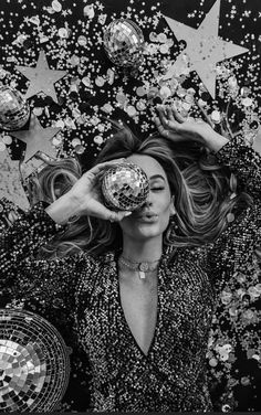 a black and white photo of a woman holding a disco ball above her head with stars in the background