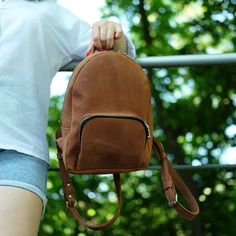 "This small leather backpack is original and stylish. It can be a great gift for yourself or a loved one as well as a stunning accessory to a family picnic or a hike. The leather backpack has a spacious main compartment and an external zippered pocket for your phone or other small items. The backpack is made of 100% leather and without pads! Size Mini: - Length  -- 8\"  (21 cm) - Height -- 10½\" (27 cm) - Width  -- 3\" (8 cm) Size XL: - Length  -- 10\" (25 cm) - Height -- 13\" (33 cm) - Width  -- 4½\" (12 cm) Other backpack in our shop : https://etsy.me/2yIdw2Q ✔✔HOW TO ORDER PERSONALIZATION? ✔✔ If you want any logo or image please send me it before ordering in the message. I will answer as soon as possible, I can make it or not. 1. If you want Personalization - choose \"Size + Personalize Leather Softback School Backpack, Leather Softback Backpack For Back-to-school, Leather-backed Backpack Shoulder Bag For Trips, Brown Faux Leather Backpack For On-the-go, Brown Leather Backpack With Gold-tone Hardware, Casual Brown Leather Backpack With Anti-theft Pocket, Brown Leather Backpack With Adjustable Strap For On-the-go, Small Leather Backpack, Girls Backpack