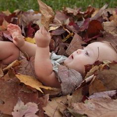 a baby is laying in leaves on the ground with his hand up to its head