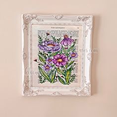 an old book with flowers painted on it is hanging on the wall in front of a white frame