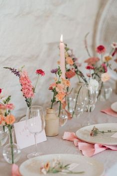 the table is set with pink and orange flowers in glass vases, plates, and candles