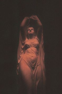 a statue is shown in the dark with its arms spread out and hands raised above her head