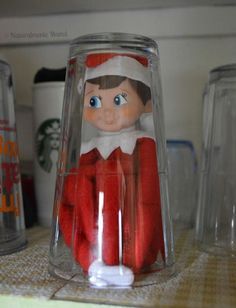 an elf doll in a glass jar on a shelf next to other cups and jars